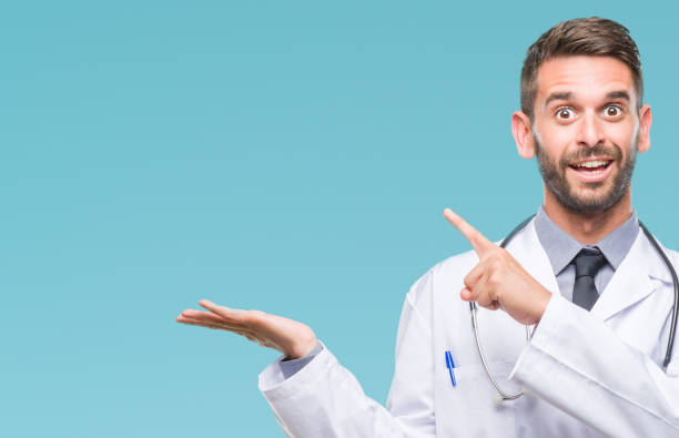 istock Young handsome doctor man over isolated background amazed and smiling to the camera while presenting with hand and pointing with finger. 1042451314