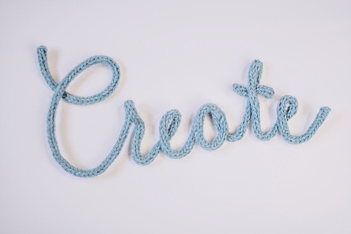 The word create formed with knit cord. Blue wool yarn knit into a cable, then formed into script typography to represent creative activities.