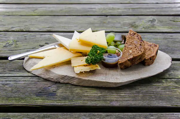 Several kinds of cheese, artisan bread, grapes and parsley on a wooden plate on an rough wooden table
