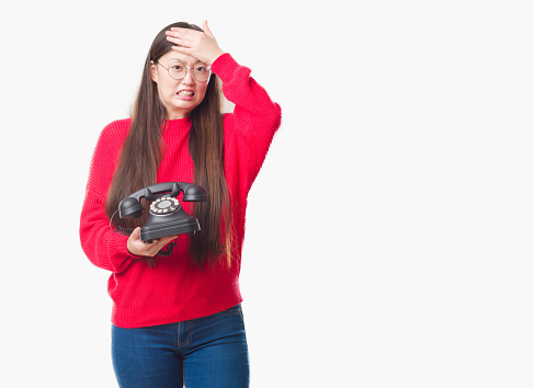 Young Chinese woman over isolated background holding vintage telephone stressed with hand on head, shocked with shame and surprise face, angry and frustrated. Fear and upset for mistake.