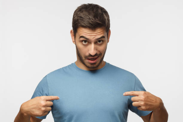 istock Young man in blue t-shirt pointing to himself with question if he did something wrong. You talking to me? 1042466092