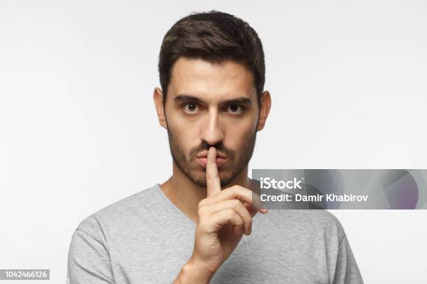 Shhh Gesture Young Man Isolated On Gray Background Dressed In White Casual Tshirt Pressing Finger To Lips As If Asking To Keep Silenc Stock Photo - Download Image Now