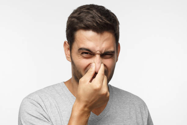close up portrait of young man holding his nose as if smelling something rotten and stinky, trying to find source of odor - facial expression unpleasant smell shirt caucasian imagens e fotografias de stock