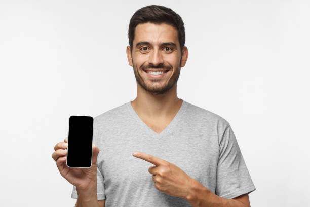 istock Young smiling man holding blank phone with empty black screen, isolated on gray background 1042466226