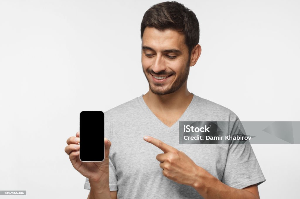 Retrato de homem feliz, demonstrando o smartphone em branco e apontando para a tela em branco vazia com sorriso. Copyspace para yor app - Foto de stock de Homens royalty-free