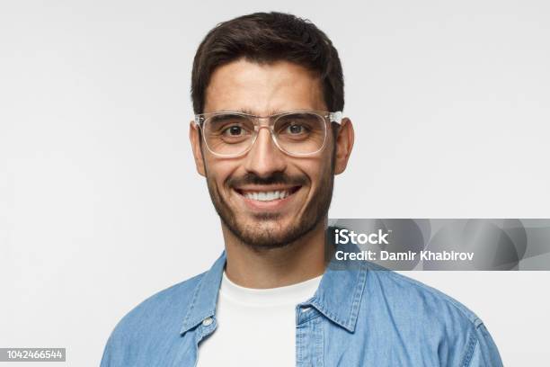 Young Positive Man With Eyeglasses Dressed In Light Blue Shirt And White Tshirt Looking At Camera With Happy Smile Isolated On Gray Background Stock Photo - Download Image Now
