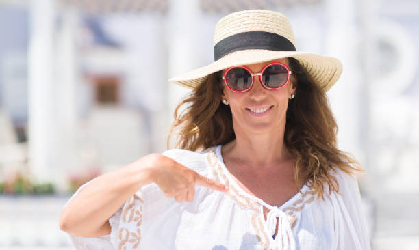 istock Middle age brunette woman wearing sunglasses and summer hat with surprise face pointing finger to himself 1042467310