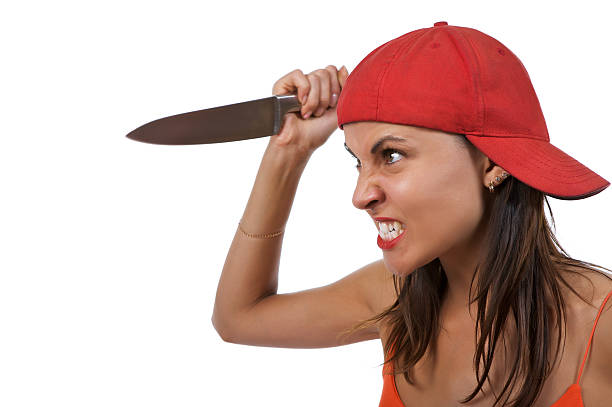 EEmotional portrait of a young woman isolated on a neutral background. Mimicking a dangerous killer, she threatens with a sharp, raised knife in her right hand while wearing a neutral and vaguely smil