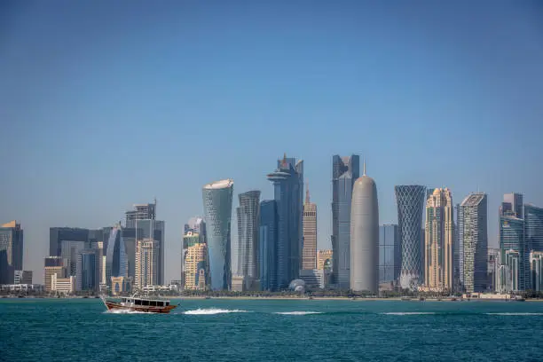 Photo of The skyline of Doha with a traditional boat in the foreground in Qatar, on a blue sky day, winter time, seen from the MIA Park