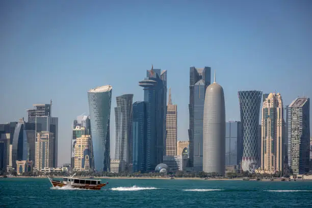 Photo of The skyline of Doha with a traditional boat in the foreground in Qatar, on a blue sky day, winter time, seen from the MIA Park