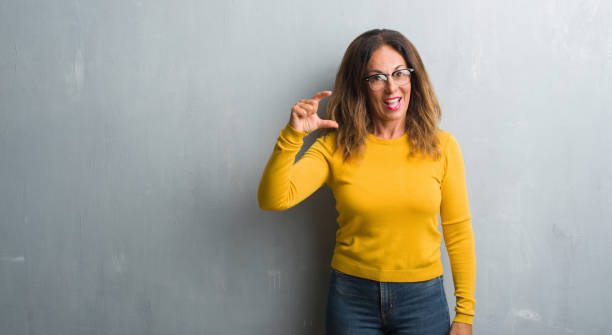 istock Middle age hispanic woman over grey wall wearing glasses smiling and confident gesturing with hand doing size sign with fingers while looking and the camera. Measure concept. 1042471280