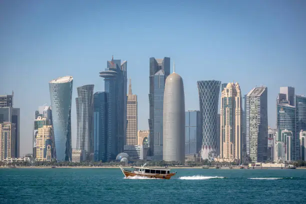 Photo of The skyline of Doha with a traditional boat in the foreground in Qatar, on a blue sky day, winter time, seen from the MIA Park