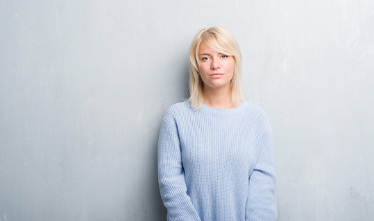 Adult caucasian woman over grunge grey wall wearing winter sweater with serious expression on face. Simple and natural looking at the camera.