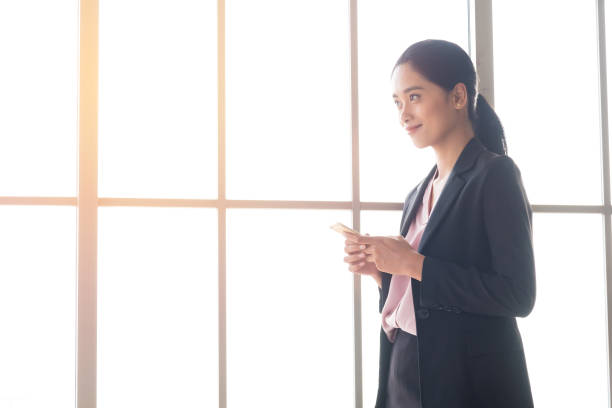 istock Smiling Young Businesswoman Using Phone By Window At Office 1042517462