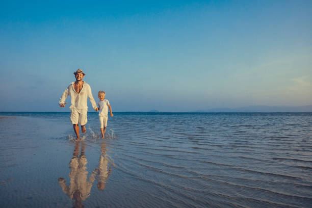 Little boy walking on the beach, holding hands with his father, man to man.