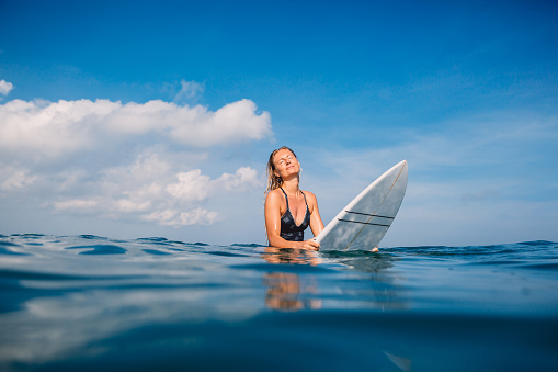 Beautiful surfer woman in swimwear with surfboard. Surfer with surfboard in tropical ocean.
