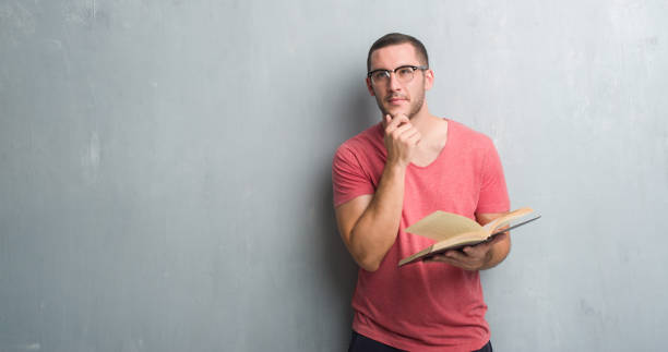 istock Young caucasian man over grey grunge wall reading a book serious face thinking about question, very confused idea 1042535844