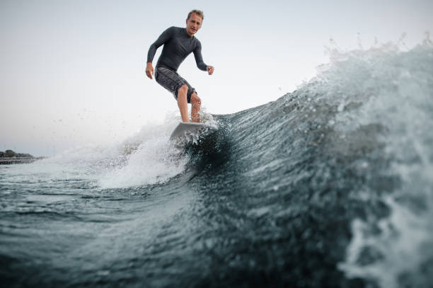 istock Blue wave on a foreground with a happy man wakesurfing down it on the background 1042539386