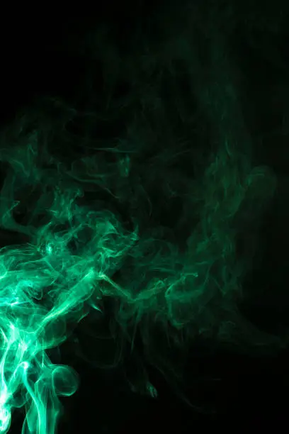 Photo of The movement of green smoke takes place on a fierce black background, fearing an abstraction on a black background.