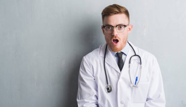 istock Young redhead doctor man over grey grunge wall scared in shock with a surprise face, afraid and excited with fear expression 1042558398