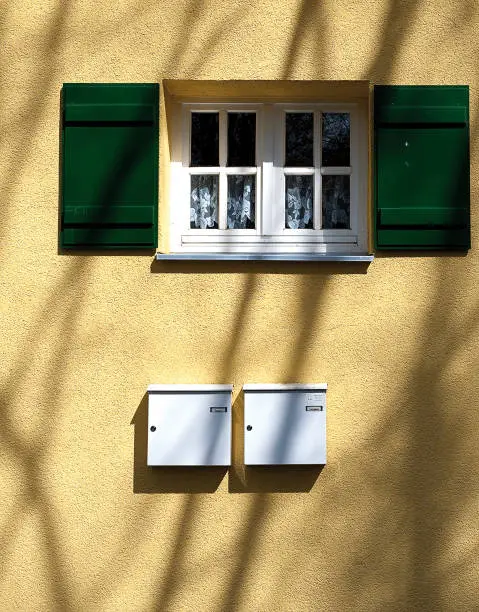 Yellow painted house wall with window and mailboxes in Munich