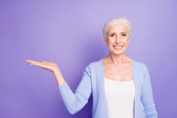 istock Grey haired old nice beautiful smiling woman holding product object, copy blank empty space. Isolated over violet purple background 1042575314