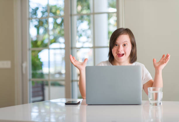 istock Down syndrome woman at home using computer laptop very happy and excited, winner expression celebrating victory screaming with big smile and raised hands 1042581344