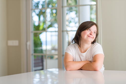 Down syndrome woman at home smiling looking side and staring away thinking.