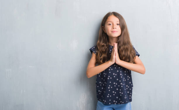 istock Young hispanic kid over grunge grey wall praying with hands together asking for forgiveness smiling confident. 1042585876