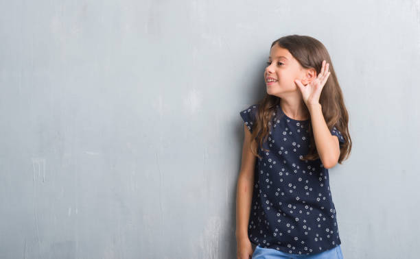 young hispanic kid over grunge grey wall smiling with hand over ear listening an hearing to rumor or gossip. deafness concept. - young ears imagens e fotografias de stock