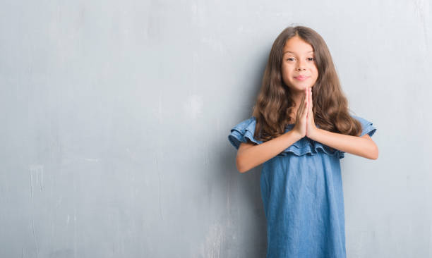 istock Young hispanic kid over grunge grey wall praying with hands together asking for forgiveness smiling confident. 1042586294