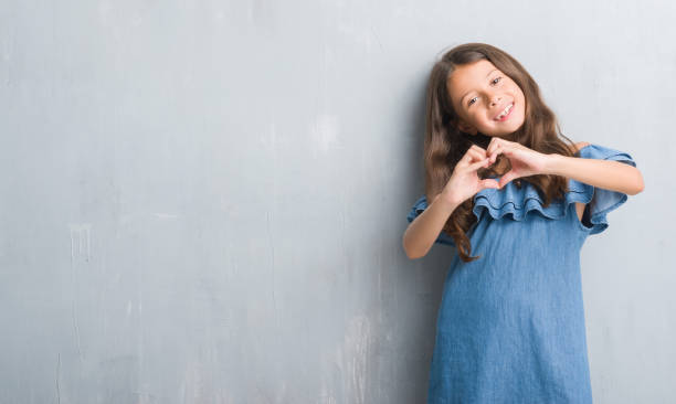 A cheerful young girl in a blue outfit posing with a red heart-shaped frame against a bright yellow background, expressing joy and creativity