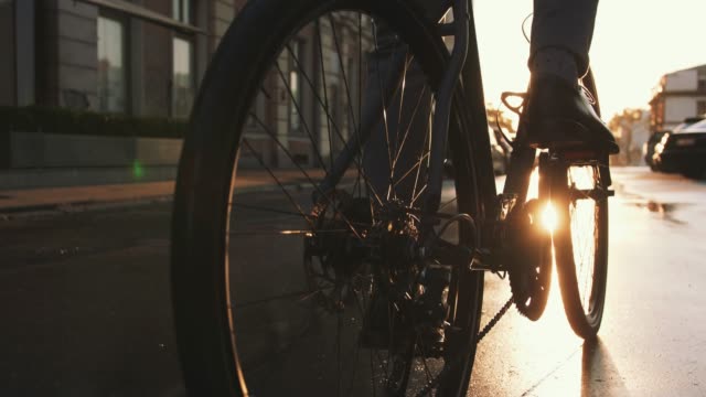 Close up shot of handsome young man driving his bicycle on the street in city center during sunrise, slow motion