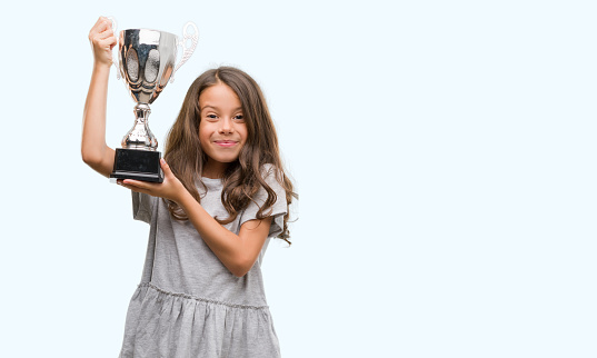 Brunette hispanic girl holding a trophy with a happy face standing and smiling with a confident smile showing teeth