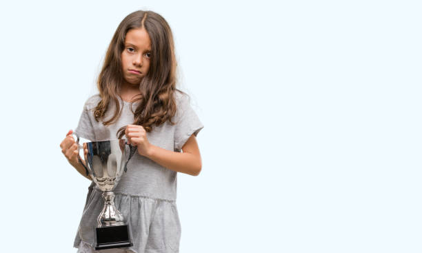 istock Brunette hispanic girl holding a trophy with a confident expression on smart face thinking serious 1042592956