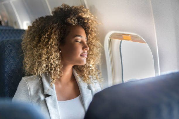 Commercial airline passenger sleeps in window seat A young woman sits in the window seat of a commercial airliner and leans back with her eyes closed. commercial airplane stock pictures, royalty-free photos & images