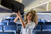 Young woman places luggage in airplane's overhead bin