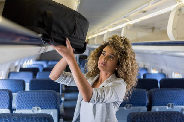 молодая женщина помещает багаж в багаж самолета - people traveling cabin baggage tourist curly hair стоковые фото и изображения