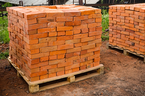 Red clay bricks are stacked on wooden pallets. Production of bricks from clay. Copy space