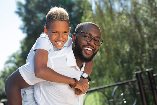 Delighted happy man carrying his son on the back Happy fatherhood. Delighted nice man smiling while carrying his son on the back african father stock pictures, royalty-free photos & images
