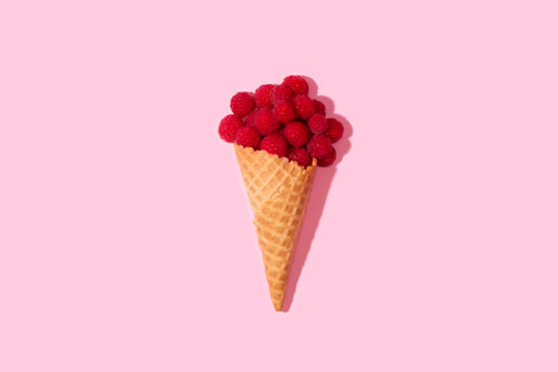 Conceptual art. Raspberries in an ice cream cone on a table on a pastel pink background. Minimal surrealism.