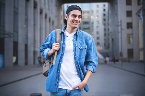 Photo of Cheerful young man with backpack enjoying walk the city