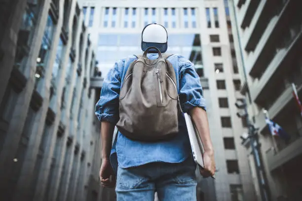Photo of Cheerful young man with backpack enjoying walk the city with laptop and snap back.