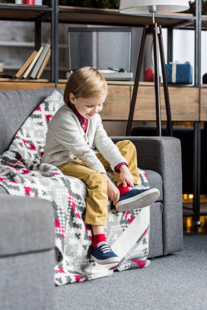 istock cute happy child sitting on couch and putting on shoe 1042653596