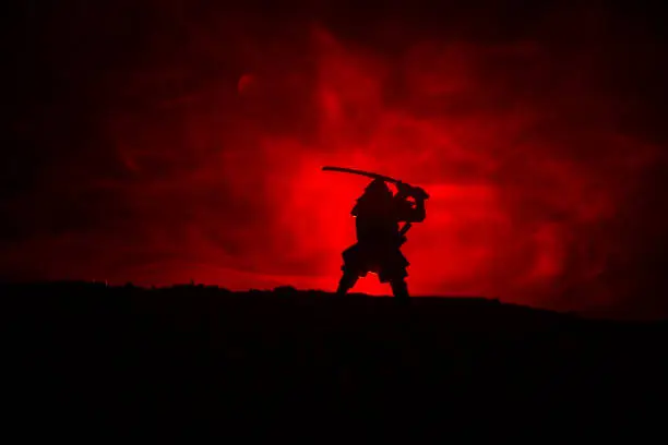 Fighter with a sword silhouette a sky ninja. Samurai on top of mountain with dark toned foggy background. Selective focus