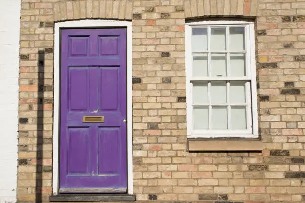 Photo of Violet pastel vintage front door on a restored brick wall of a Georgian house residential building with white wooden sash window