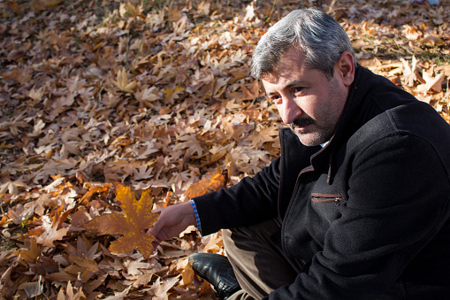 man with mustache whitened white hair sits thoughtfully in yellowed and fallen leaves