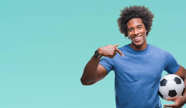 афро-американец, держащий футбольный мяч на изолированном фоне с неожиданным лицом, указывающим пальцем на себя - football human hand holding american football стоковые фото и изображения