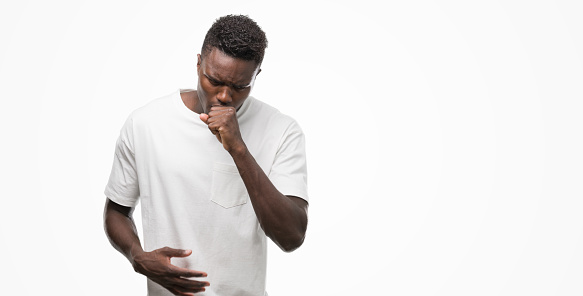 Young african american man wearing white t-shirt feeling unwell and coughing as symptom for cold or bronchitis. Healthcare concept.