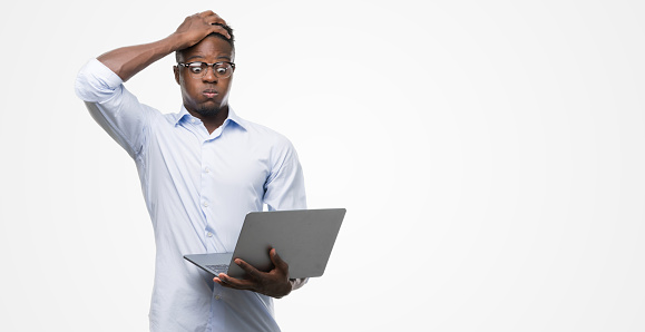 Young african american businessman using computer laptop stressed with hand on head, shocked with shame and surprise face, angry and frustrated. Fear and upset for mistake.